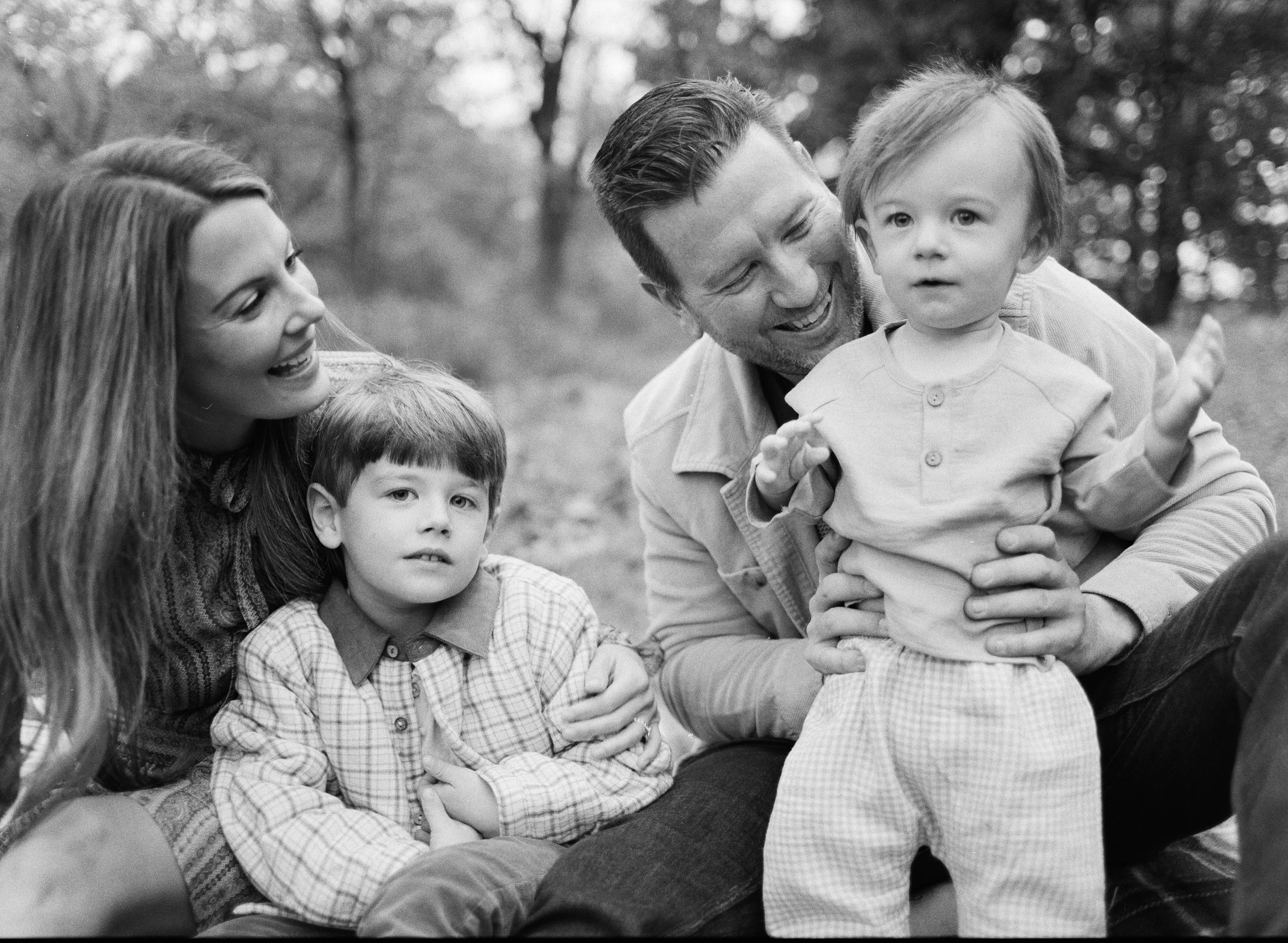 A happy family of four outdoors, with a woman, man, and two young children, smiling and enjoying time together.