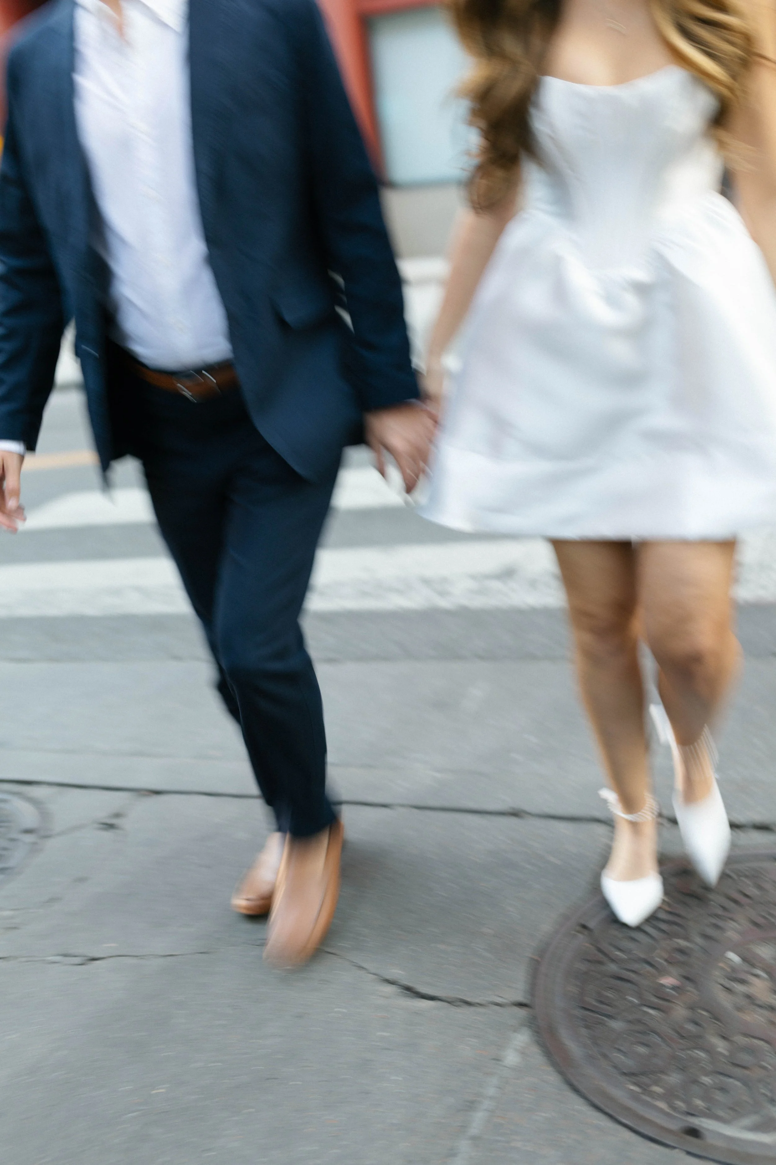 A couple holding hands crossing the street in stylish attire.