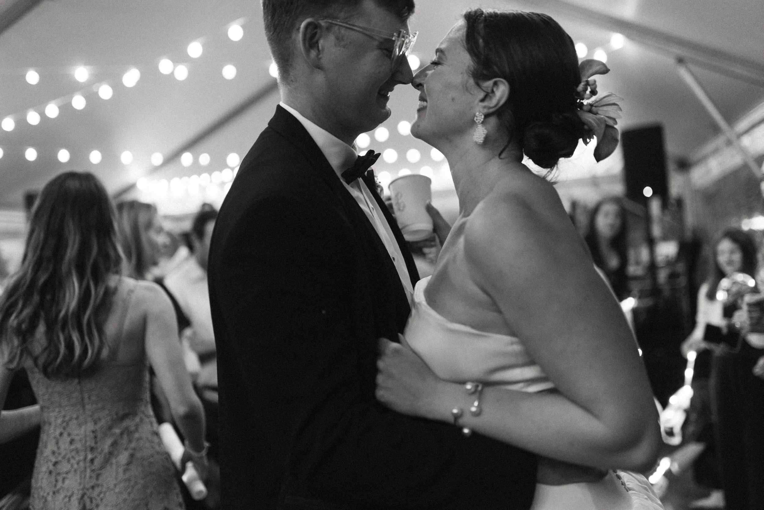 Nashville film wedding photographer. Nashville film wedding photography. A black-and-white photo of a joyful bride and groom dancing closely at their wedding reception, surrounded by guests under string lights.