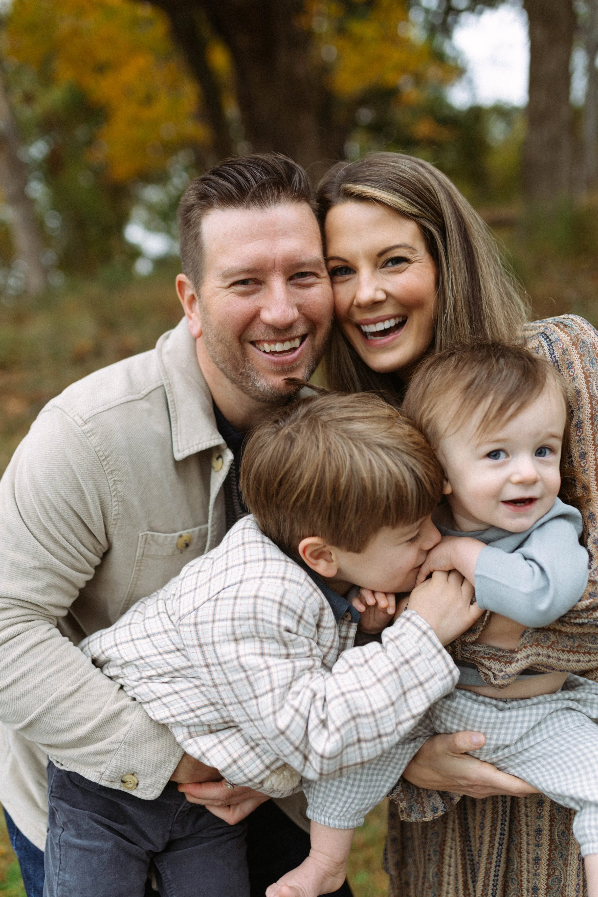 A happy family of four enjoying fall outdoors with trees and autumn leaves in the background.