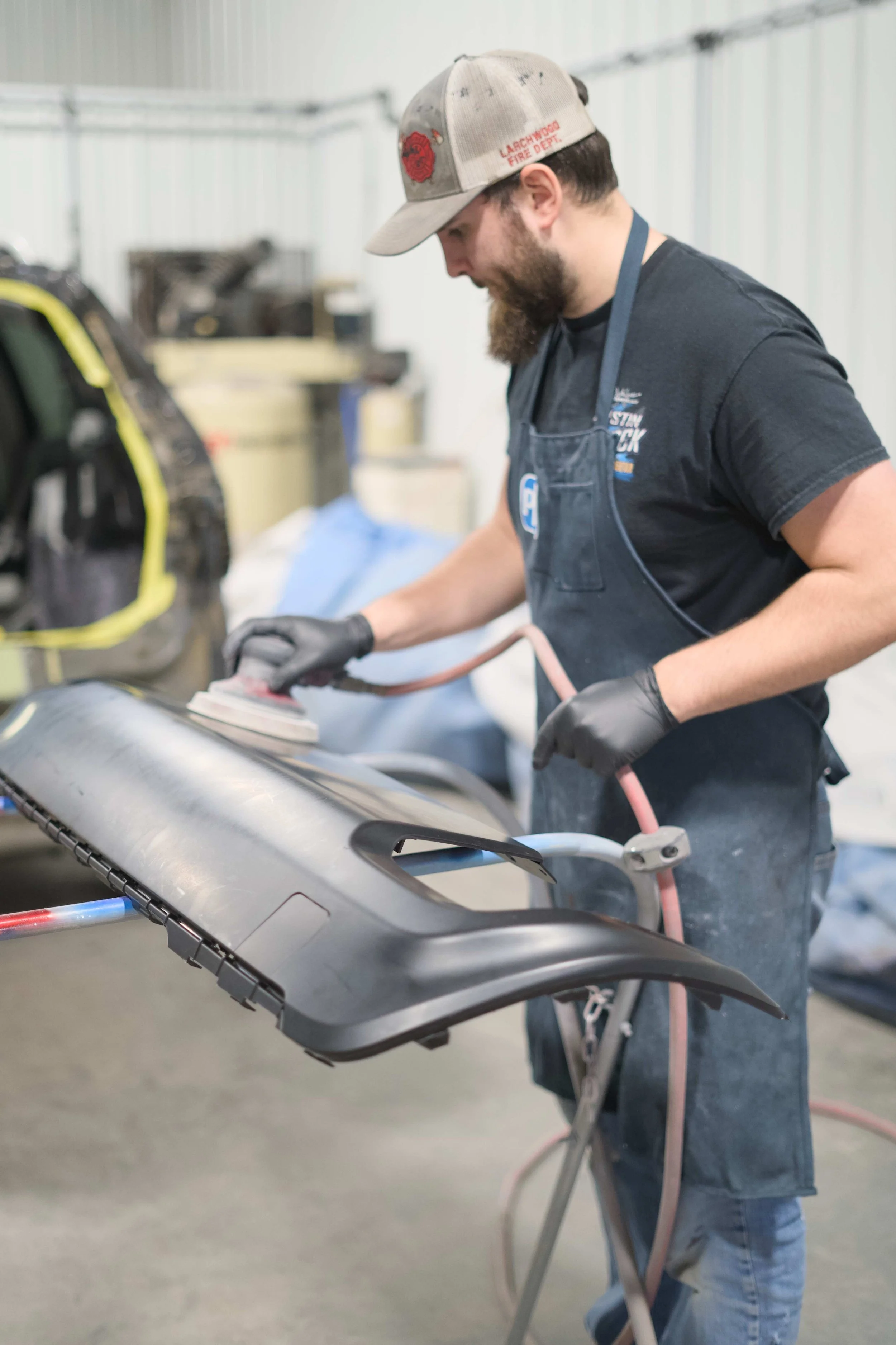 A man polishing a gray automotive part with a power buffer in a workshop.