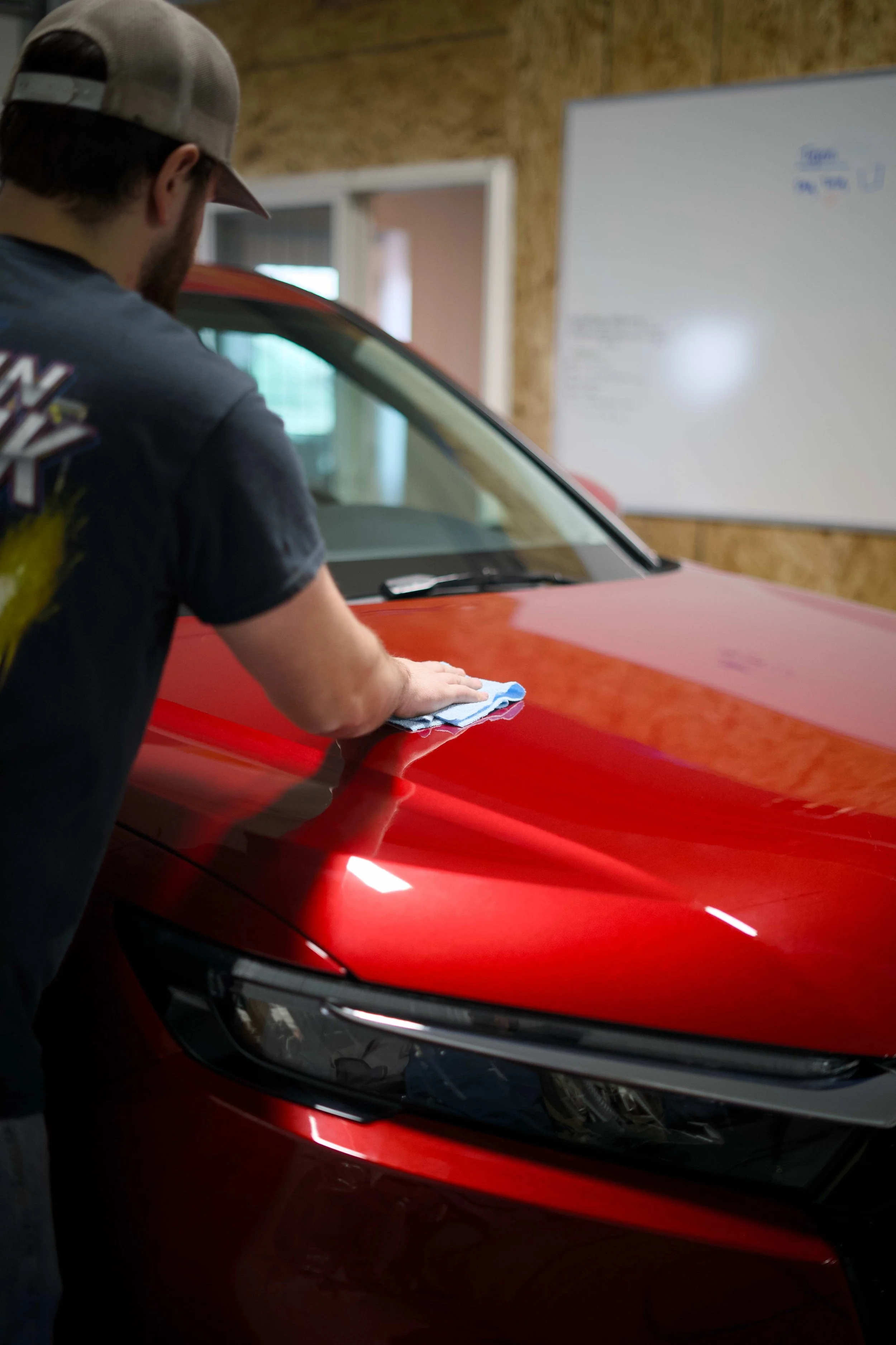 A person cleaning the hood of a red car with a cloth in a garage.