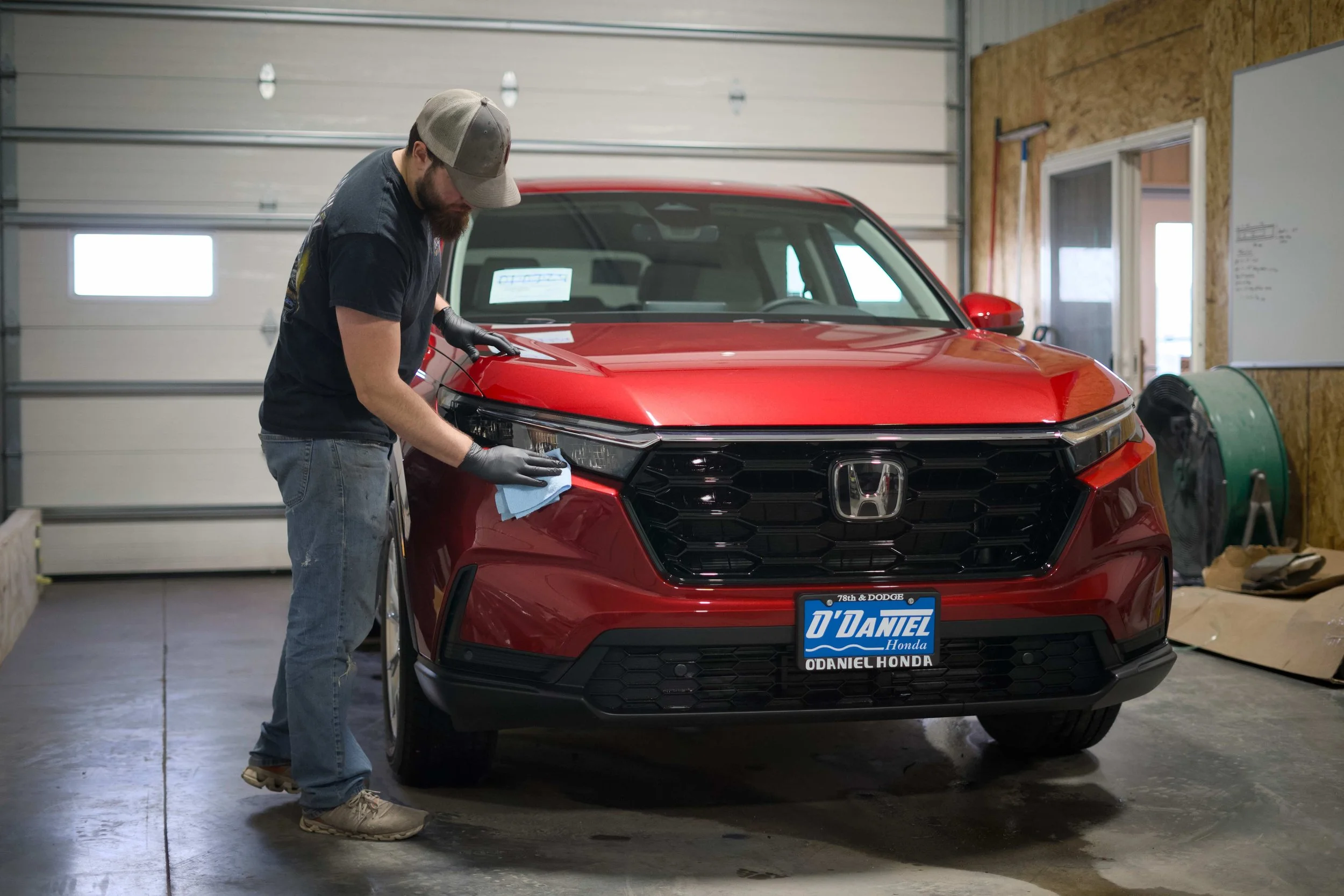 A man cleaning the front of a red Honda SUV inside a garage.