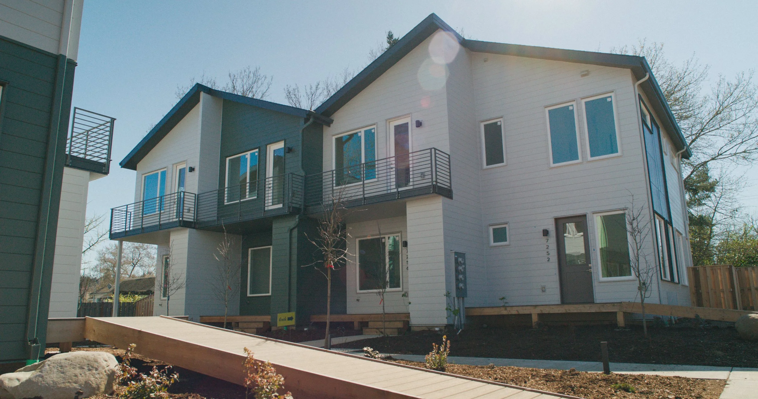 Modern multi-story residential building with balconies and large windows, under construction in a suburban neighborhood.