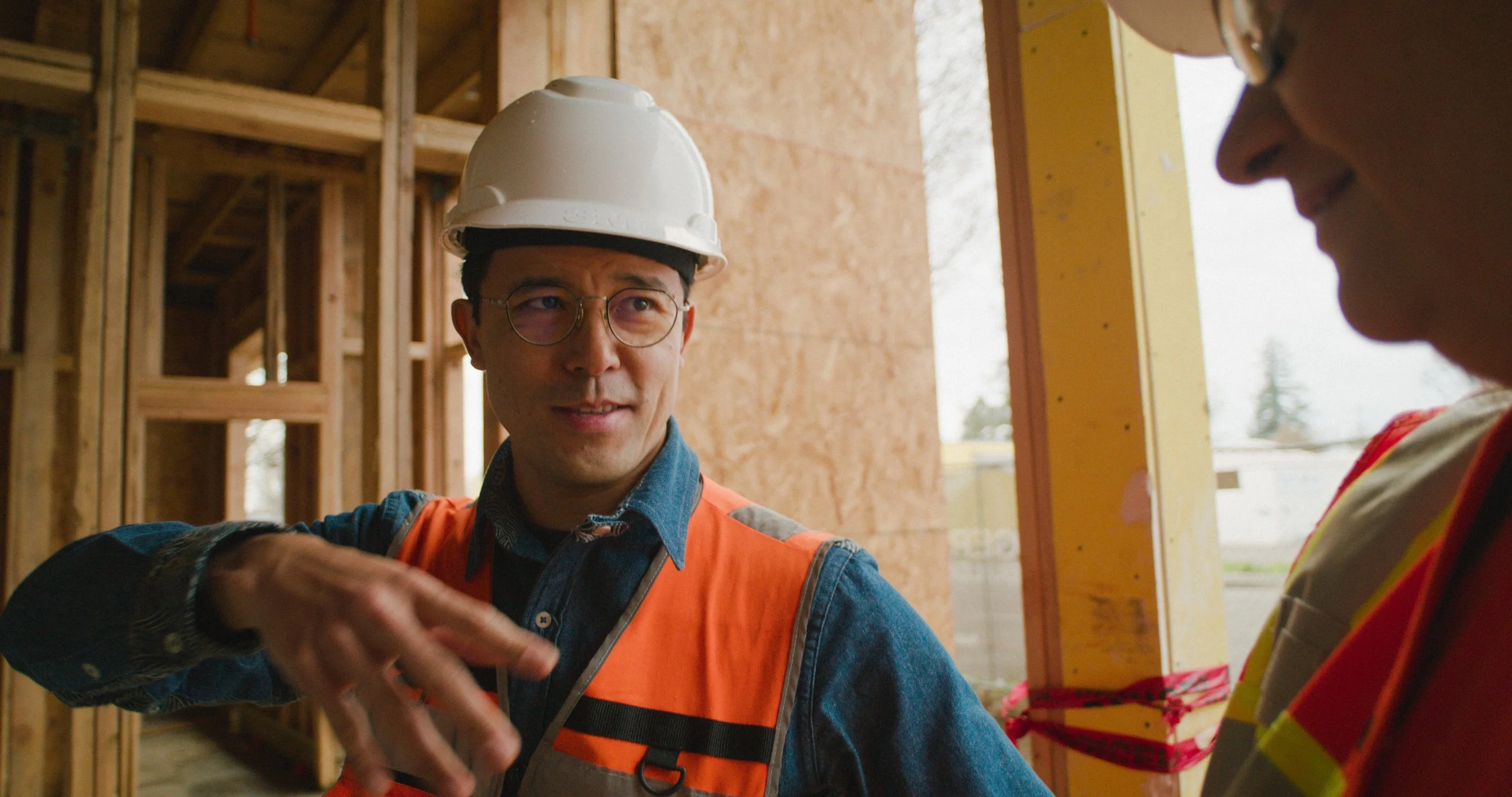 Two construction workers wearing helmets and safety vests, engaged in conversation inside a building under construction.