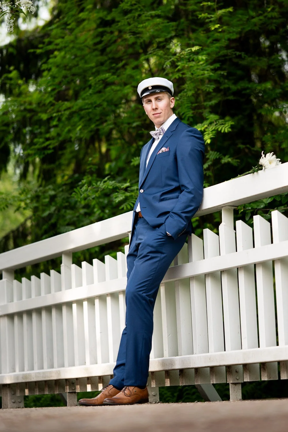 Ylioppilas nojaa valkoiseen aitaan, ylioppilaskuva miljöössä