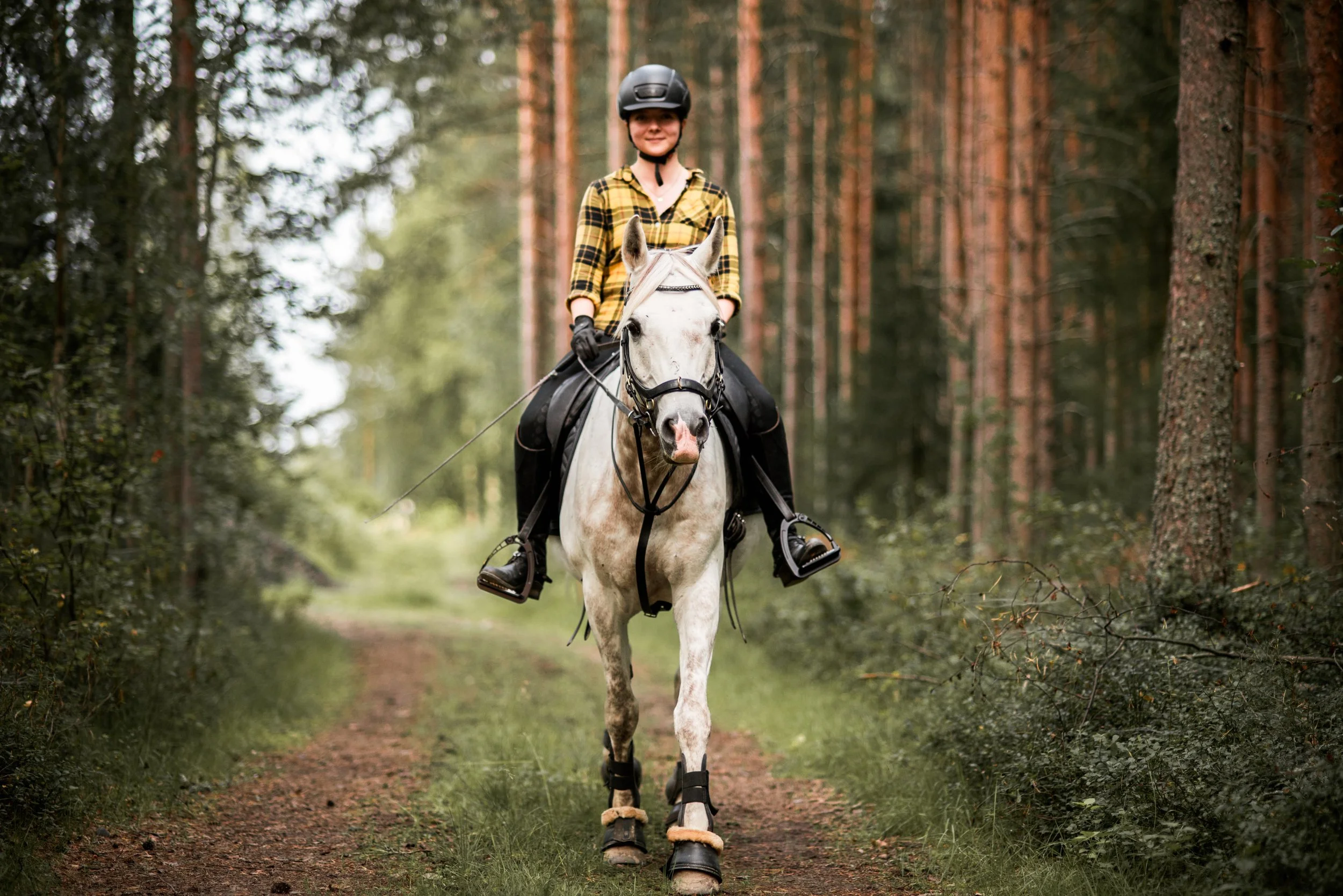 Nainen ratsastaa hevosella kohti kameraa metsässä