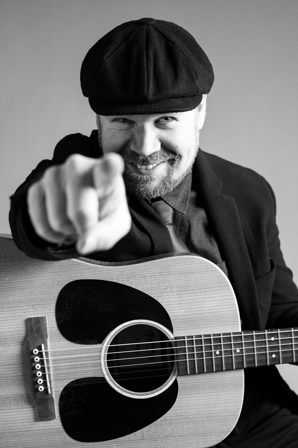 Potretti studiossa, mies pitää kitaraa ja osoittaa kameraan, mustavalkokuva