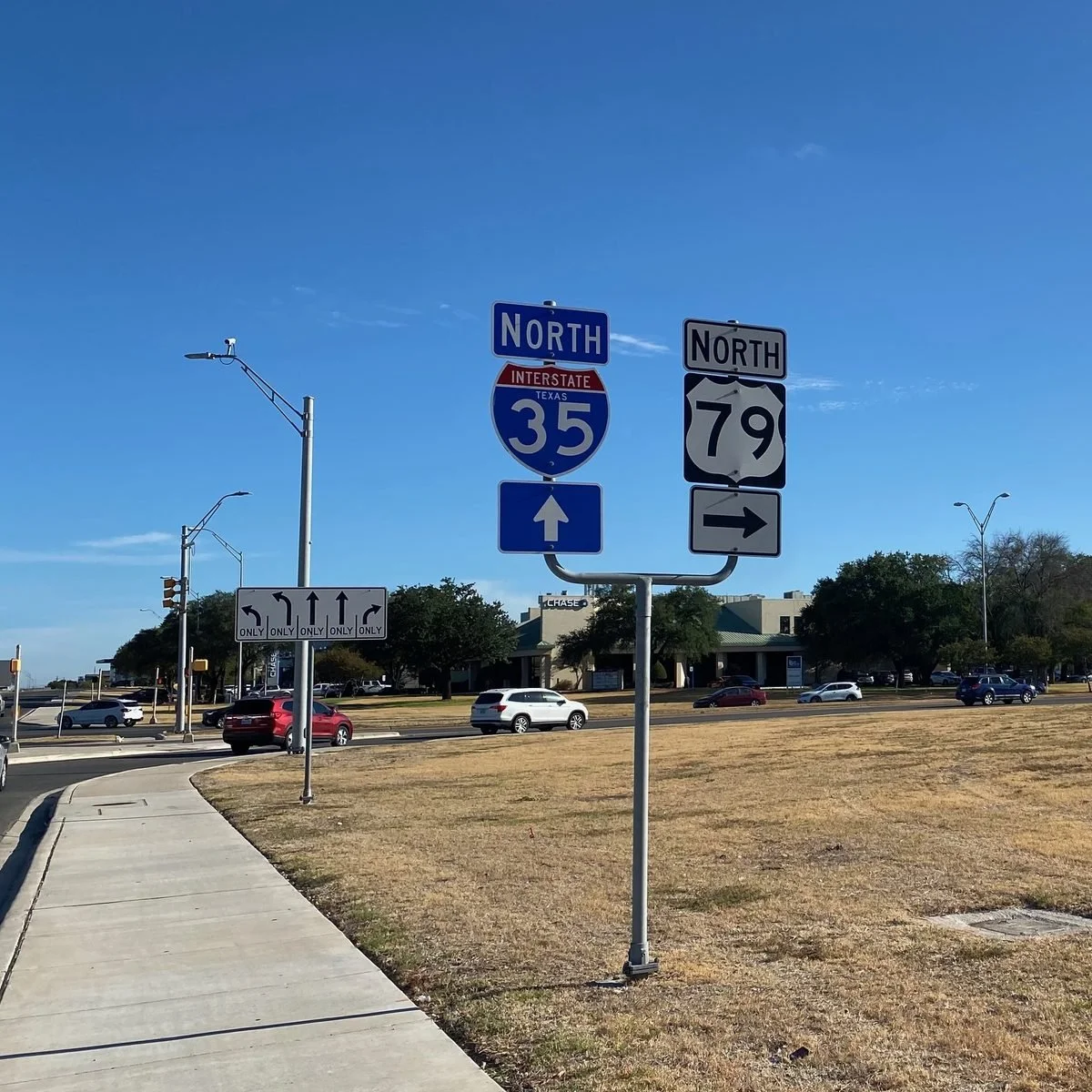 Traffic signs indicating north on Interstate 35 and Route 79, with lane arrows and parking lot in background on sunny day.