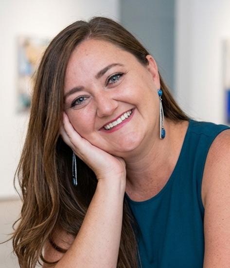 woman with brown hair, smiling with her head leaning on her hand
