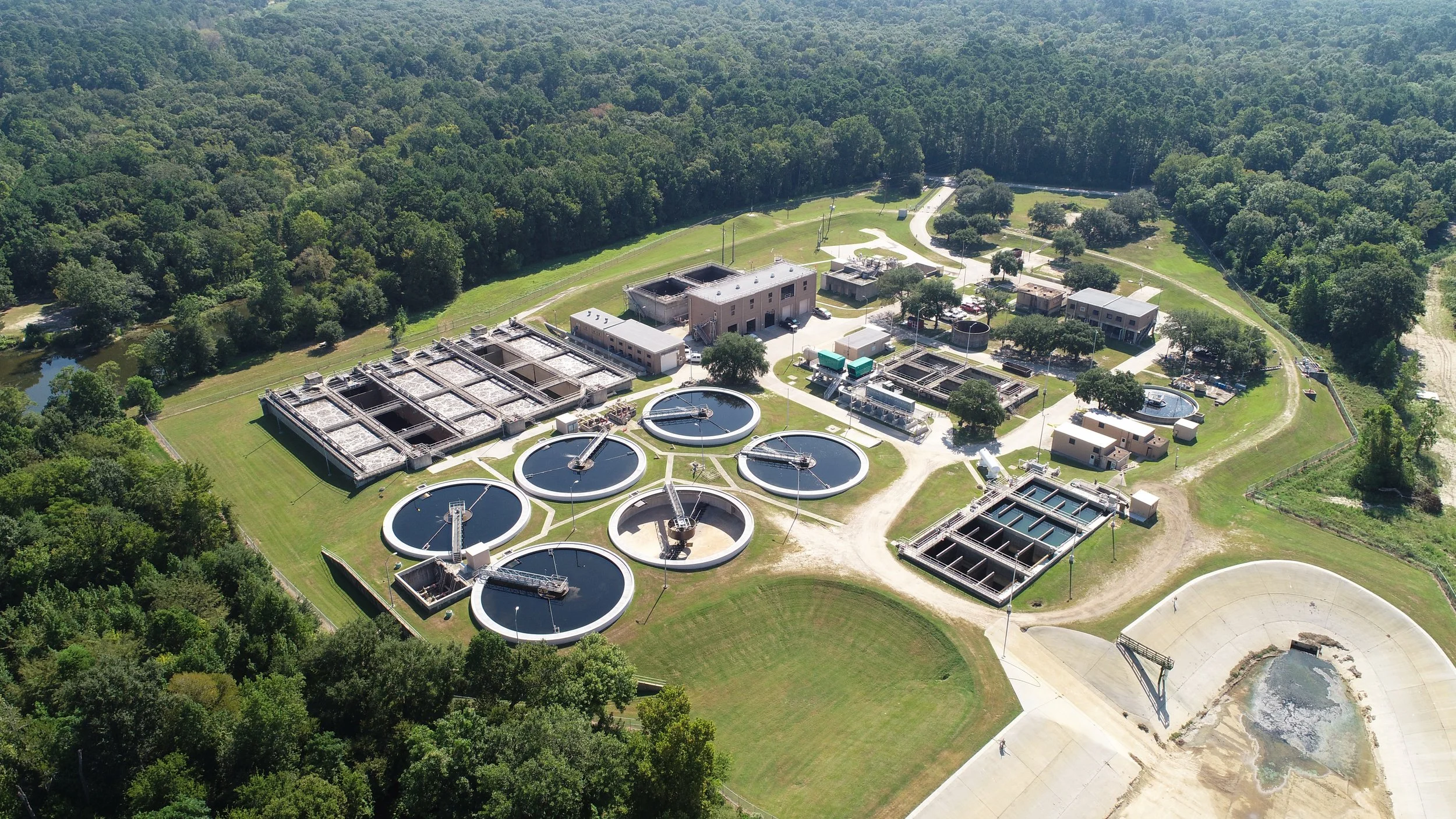 Aerial view of a full wastewater treatment plant, surrounded by grass and trees. 