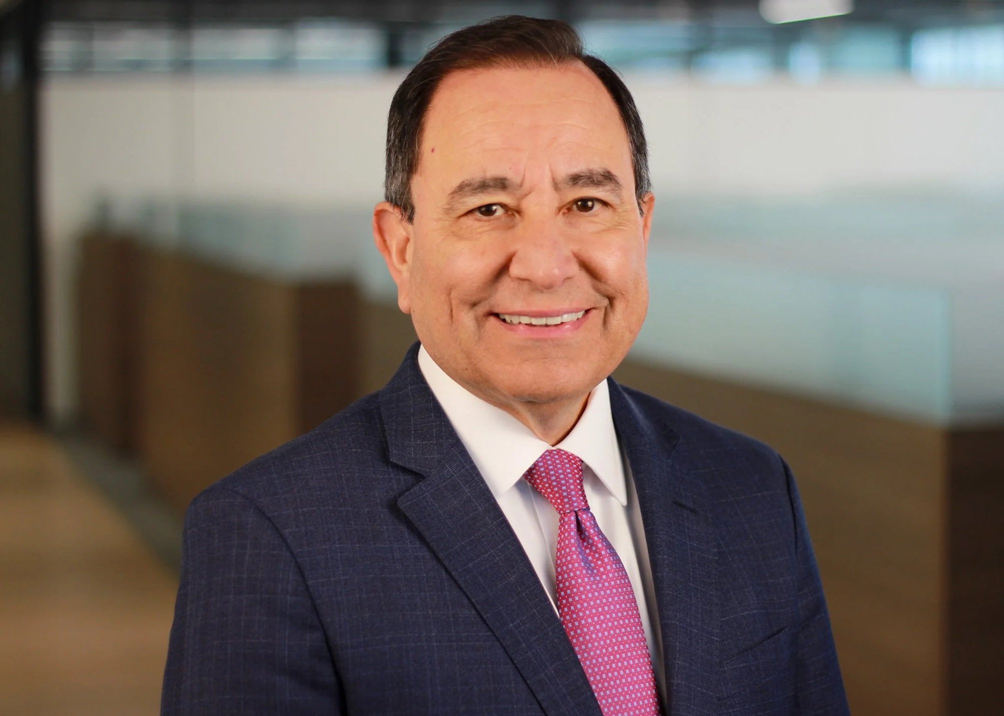Portrait of a middle-aged man in a suit and tie, smiling, in an office setting.