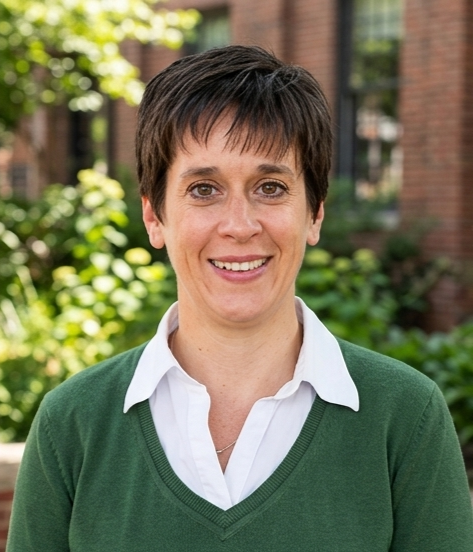 woman in green shirt with white collor standing in front of a nature landscape