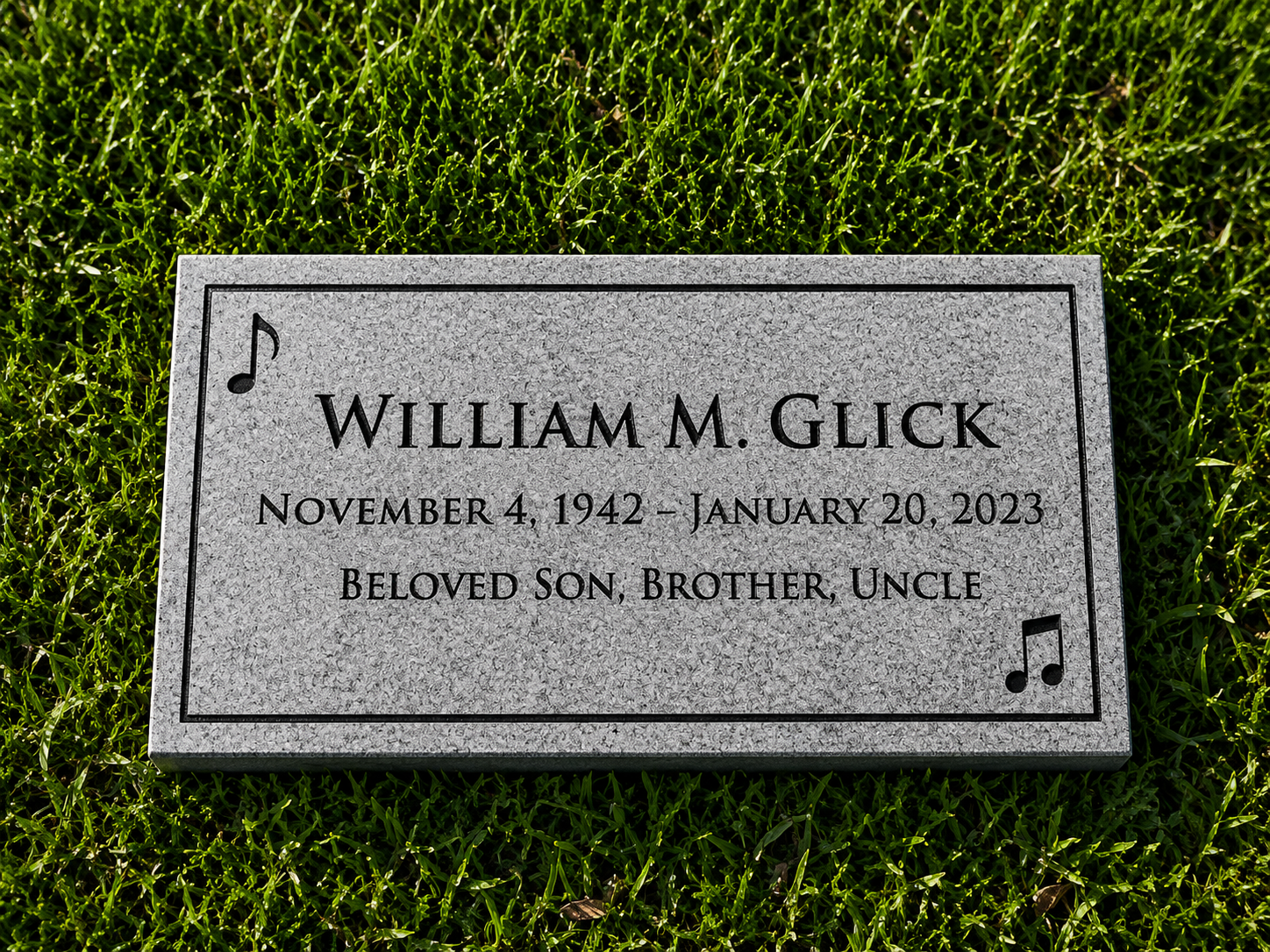 Gravestone for William M. Glick with his birth and death dates, and the words 'Beloved Son, Brother, Uncle', decorated with musical notes, set in grass.