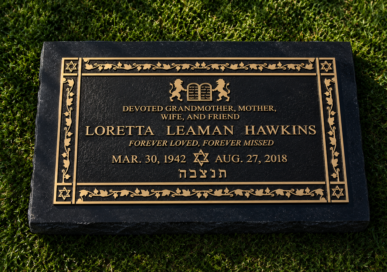Black gravestone with gold accents, dedicated to Loretta Leaman Hawkins, features Star of David and Hebrew text, surrounded by green grass.