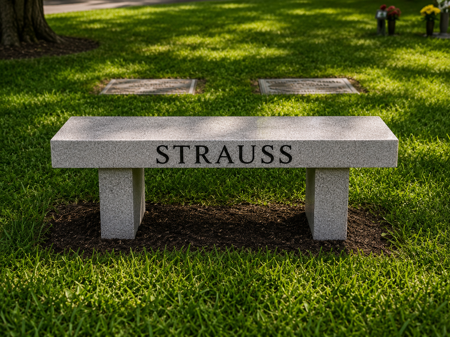 Granite memorial bench with the name 'STRAUSS' engraved on the front, situated on a grassy area in a cemetery with other plaques and memorials in the background.