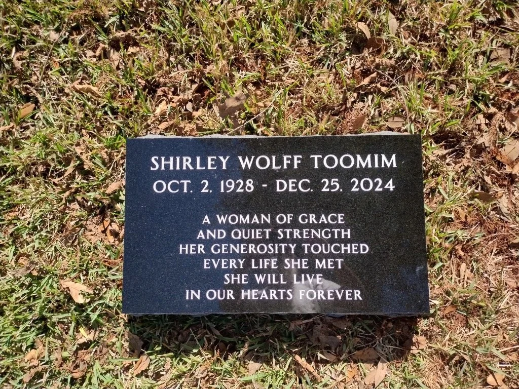 Gravestone for Shirley Wolff Toomim with birth and death dates, surrounded by grass and fallen leaves.