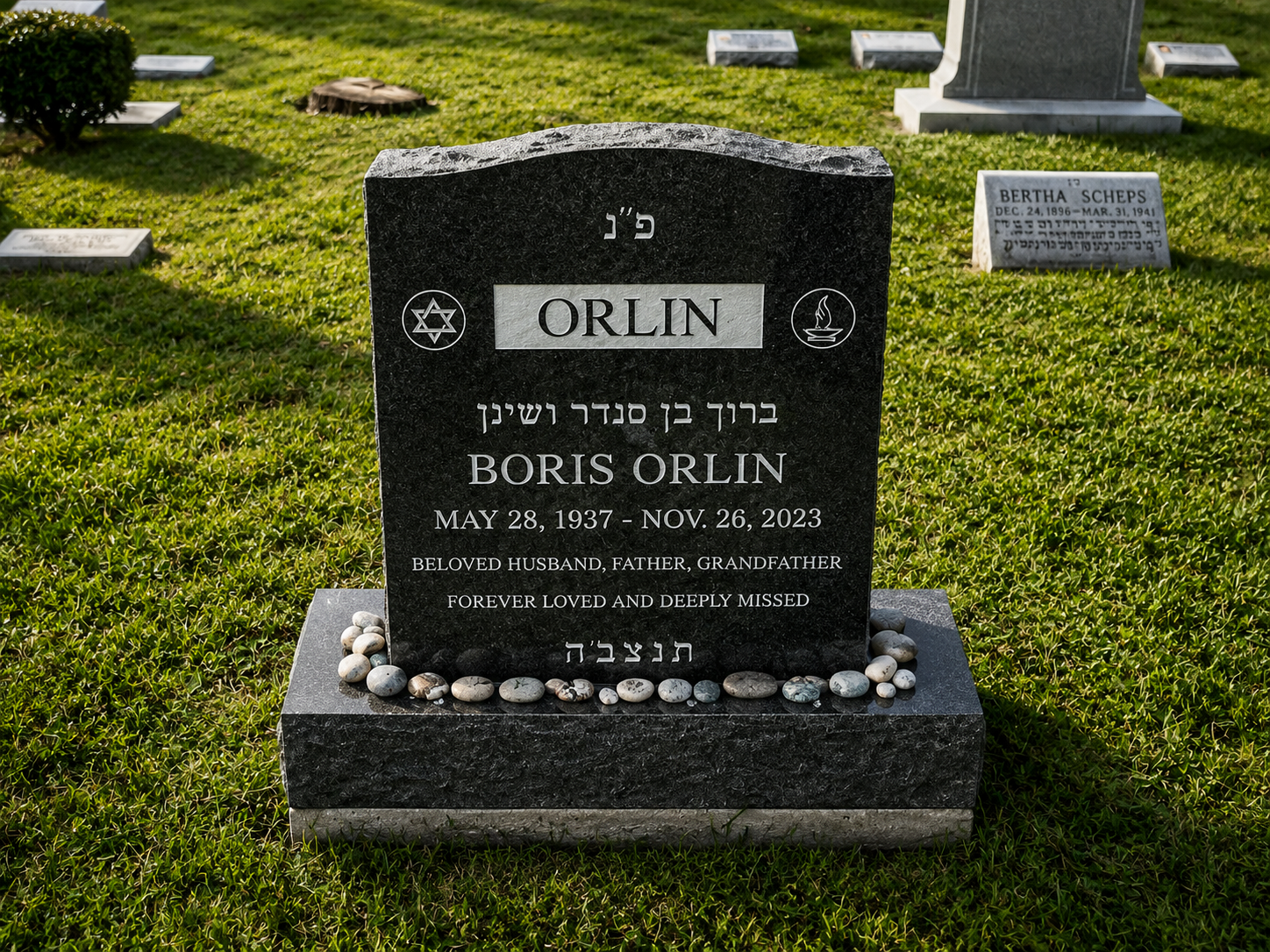 Gravestone in a cemetery for Boris Orlin, with his dates, and symbols for Judaism and flame, surrounded by small rocks, with other gravestones in the background.