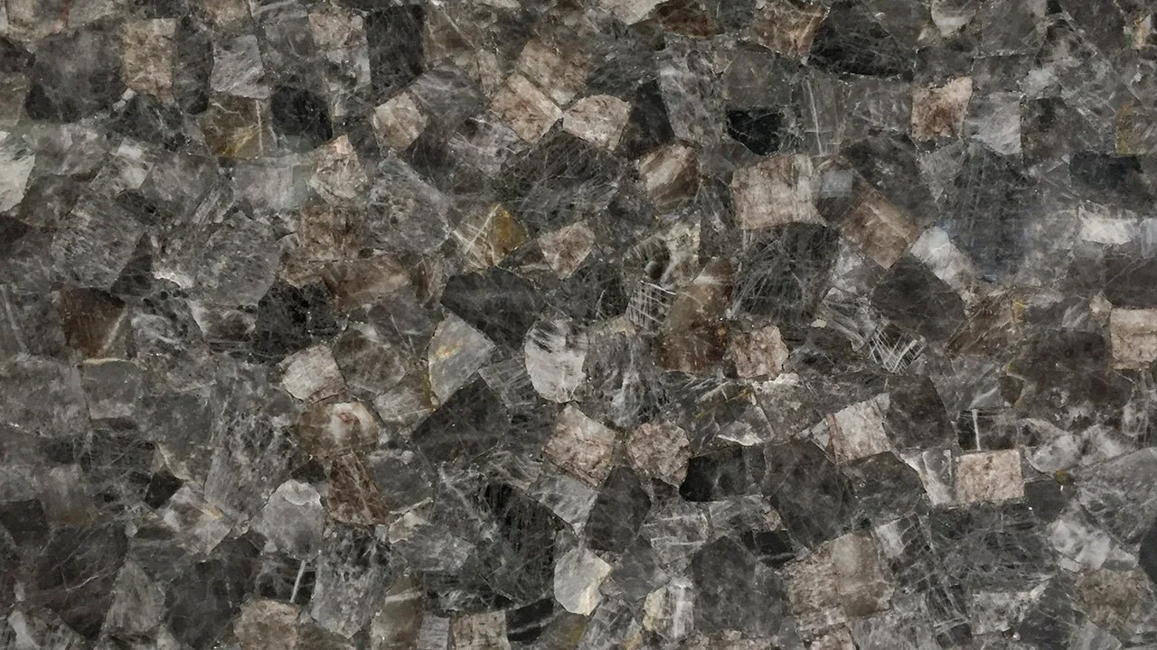 Close-up of a granite countertop with a polished surface, displaying a pattern of various shades of brown, black, and gray in a mosaic of small, irregularly shaped pieces.