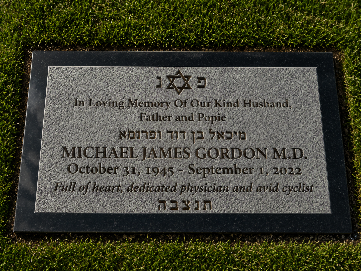 A grave marker with engraved text honoring Michael James Gordon M.D. 1945-2022. It features a Star of David at the top and Hebrew characters, and is surrounded by green grass.