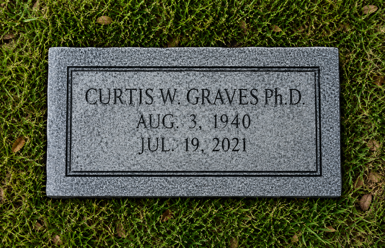 Gravestone engraved with the name Curtis W. Graves Ph.D., born August 3, 1940, died July 19, 2021, surrounded by green grass.