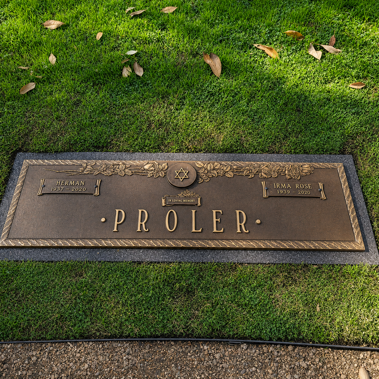 Gravestone with the name Proler at a cemetery, surrounded by green grass and fallen leaves.