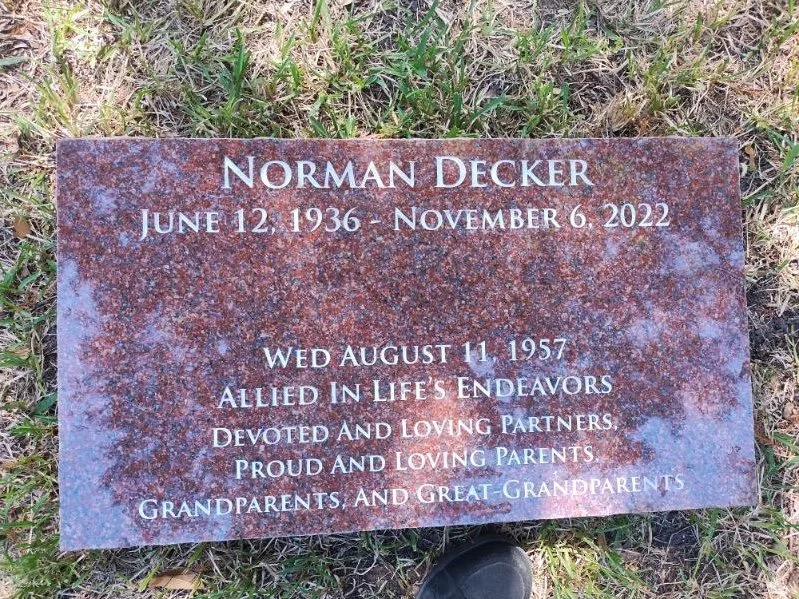 A grave marker with a granite surface engraved with the name Norman Decker, his birth date June 12, 1936, and death date November 6, 2022. The marker also includes his wife's birth date August 11, 1957, and a message honoring his life, partner, parents, and grandparents.