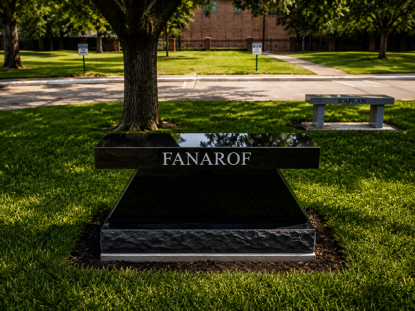 Black granite memorial plaque with the name 'FANAROF' in front of a tree, with a sidewalk and bench in the background, in a grassy park area.