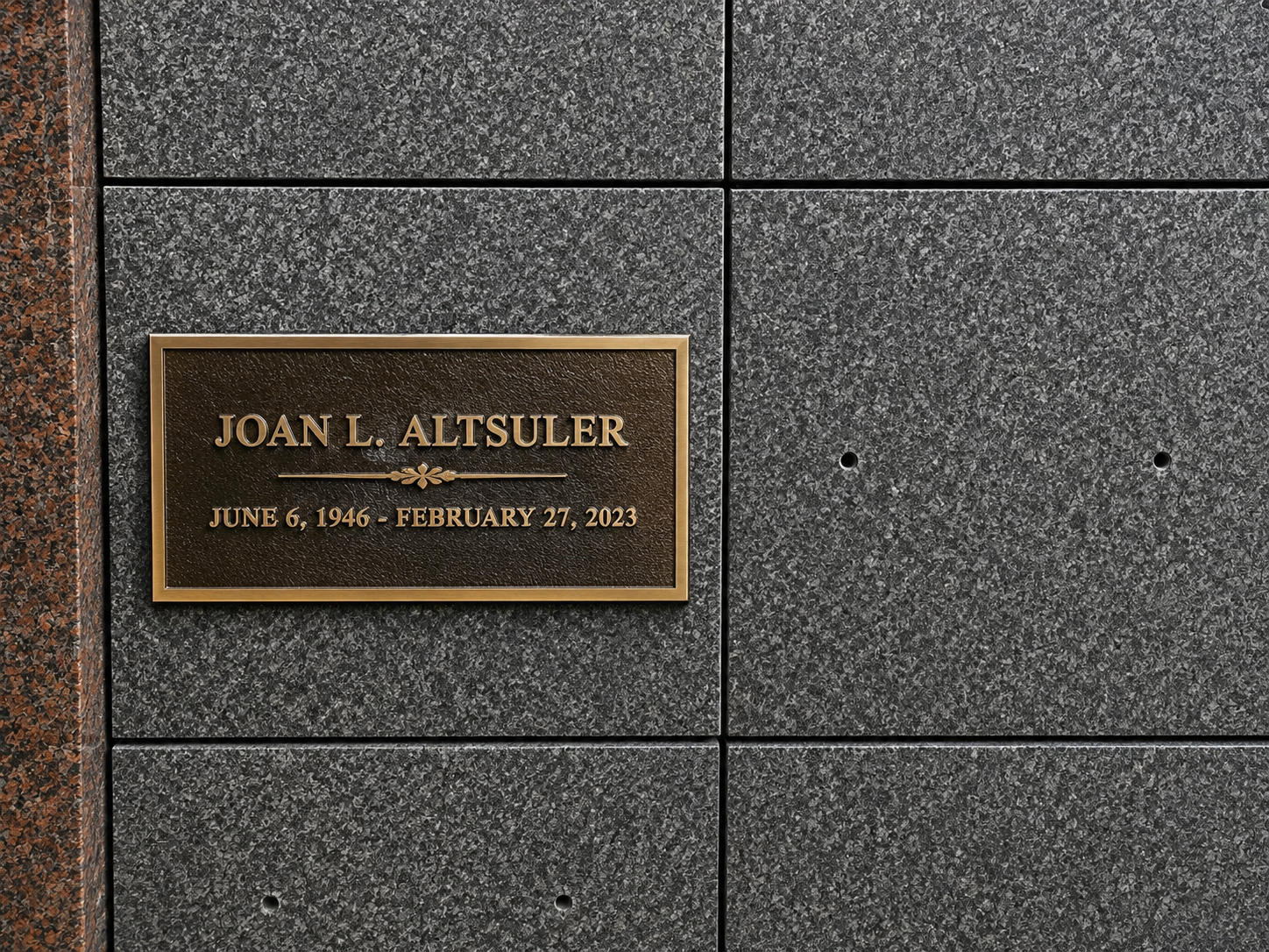 Memorial plaque for Joan L. Altsuler on a dark gray granite wall, with her birth and death dates.