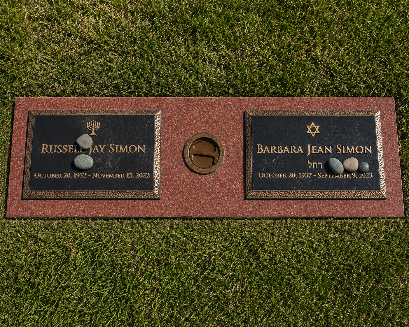 Gravestone with two plaques for Russell Jay Simon and Barbara Jean Simon, surrounded by grass, with small rocks placed on each plaque