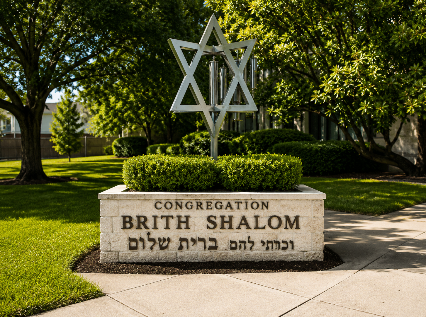 A sign reading 'Congregation Birth Shalom' in English and Hebrew, with a Star of David sculpture and wind chimes, surrounded by green bushes and trees in a well-maintained outdoor area.