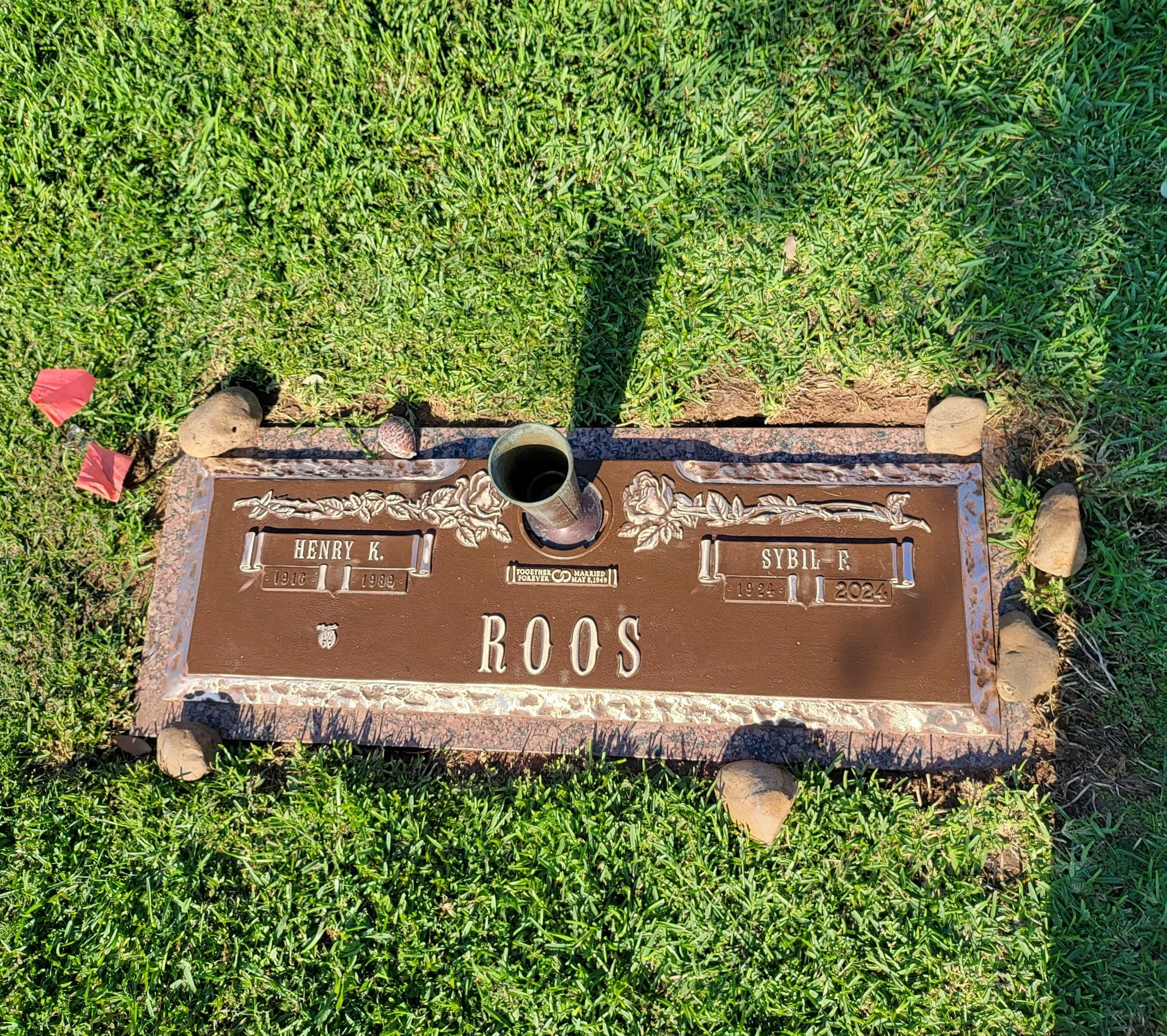 Bronze gravestone surrounded by grass and small rocks, with a candle holder on top.