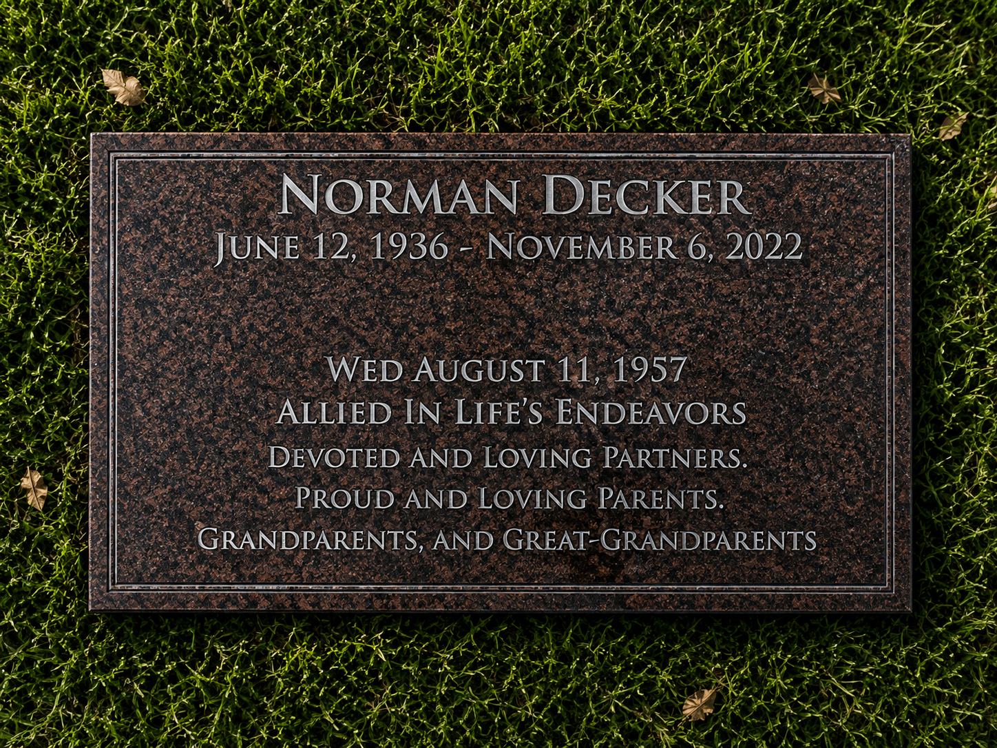 Gravestone memorial plaque for Norman Decker with birth and death dates and a message of remembrance, surrounded by green grass.