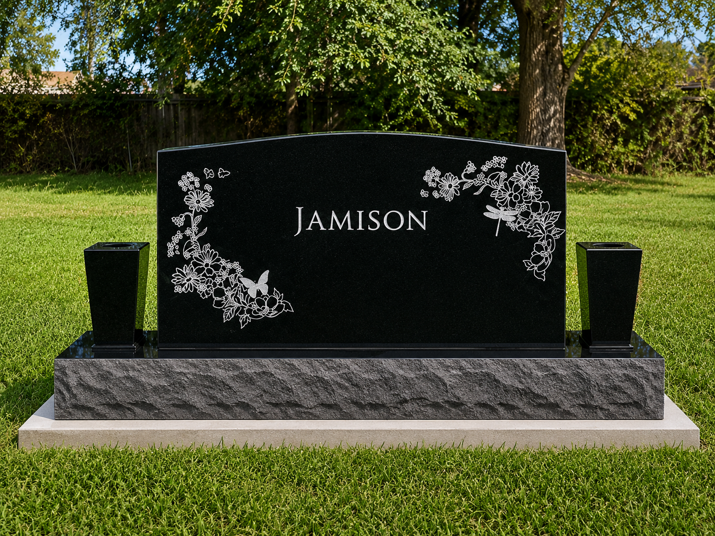 Black granite headstone with white floral and butterfly engravings, inscribed with the name 'Jamison', placed on a concrete foundation in a grassy cemetery with trees in the background.