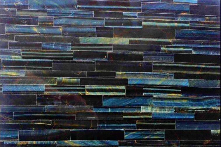 Close-up of a wall made of iridescent, rectangular tiles in shades of blue, green, and black.