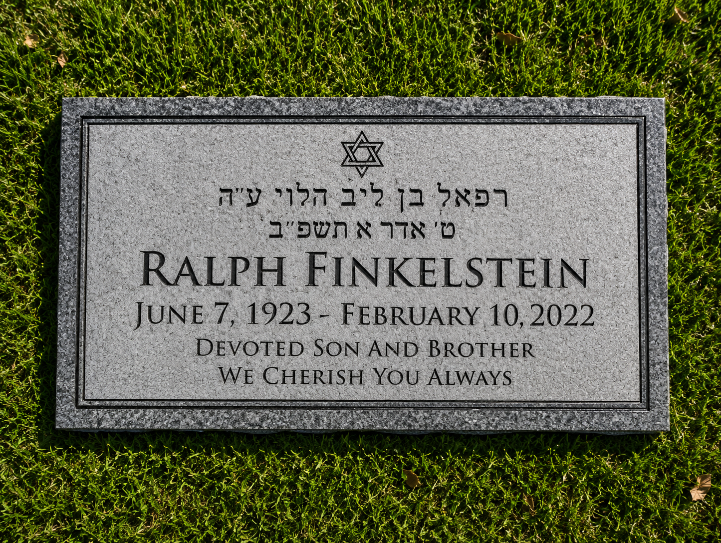 Gravestone with Star of David at top, inscribed with Hebrew text and English text honoring Ralph Finkelstein, who was born June 7, 1923, and died February 10, 2022. The gravestone is on grass.