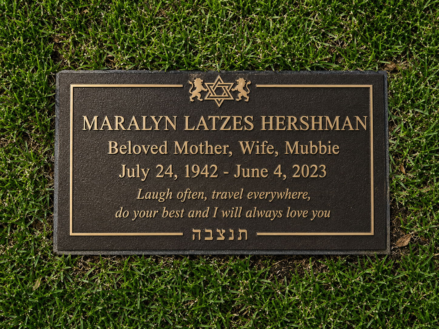 Gravestone memorial plaque for Marilyn Latzes Hershman with gold lettering, decorative top with lions and Star of David, set on green grass.
