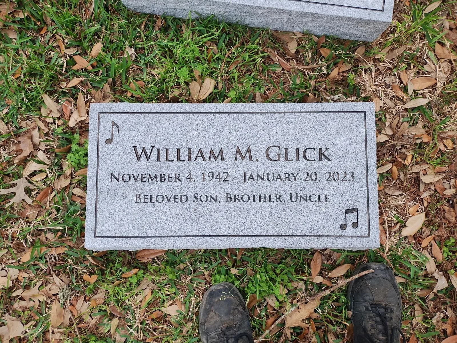 Gravestone with musical note symbols, engraved with the name William M. Glick, born November 4, 1942, and died January 20, 2023. It describes him as a beloved son, brother, and uncle.