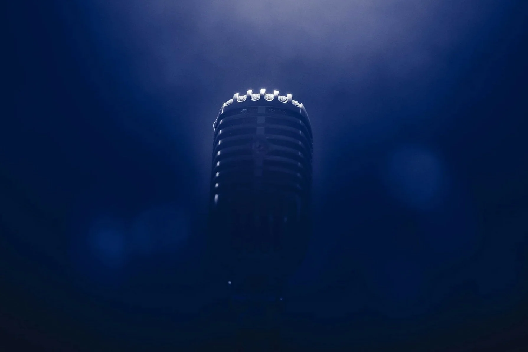 A vintage microphone illuminated by light, set against a dark background.