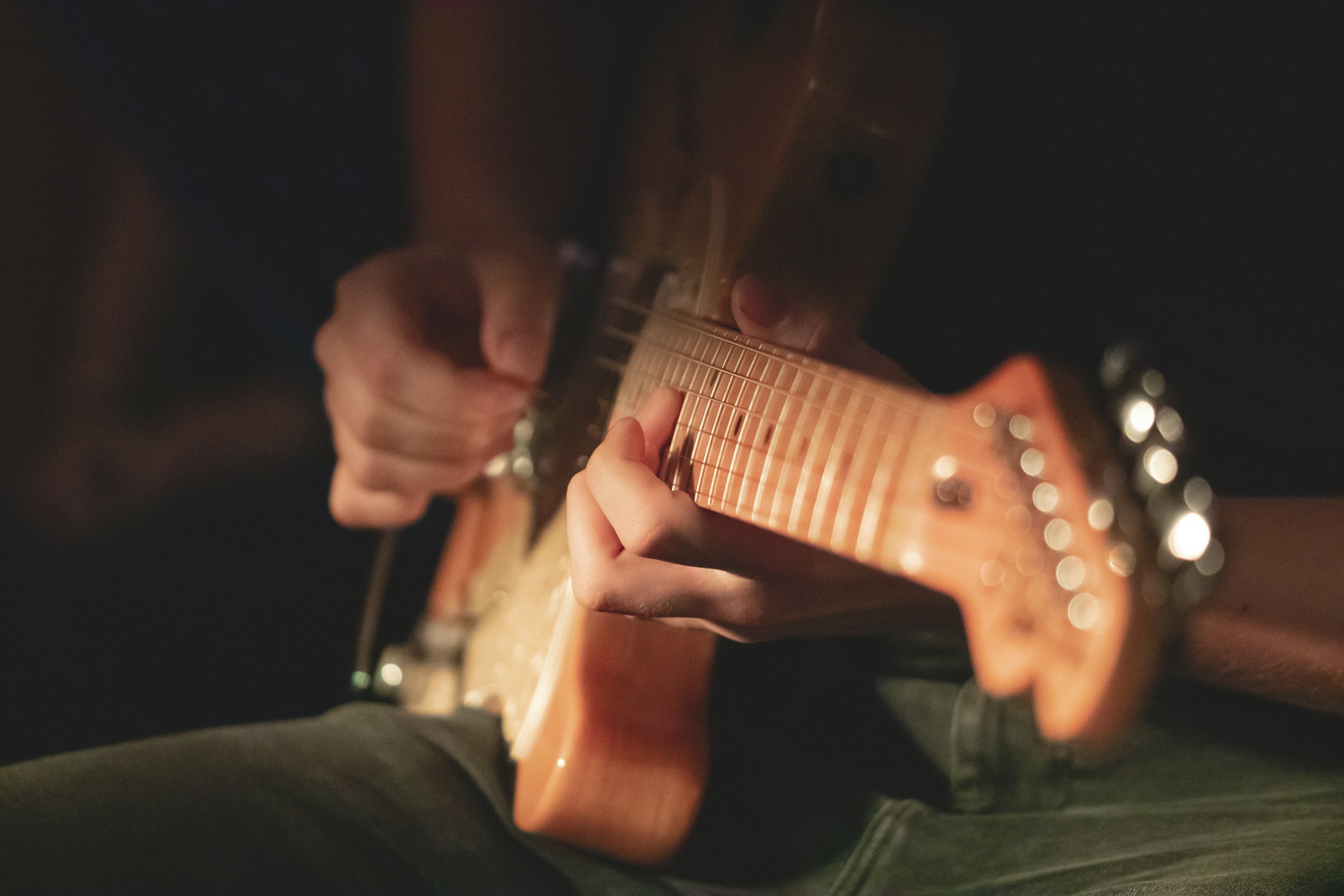 Close-up of a person playing an electric guitar, with focus on their hand on the fretboard.