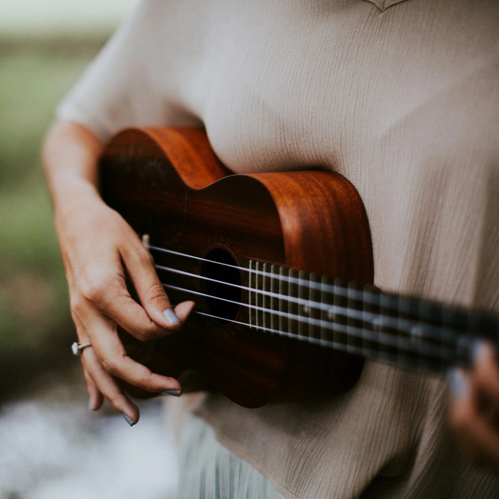 Person holding and playing an acoustic guitar, wearing a beige sweater.
