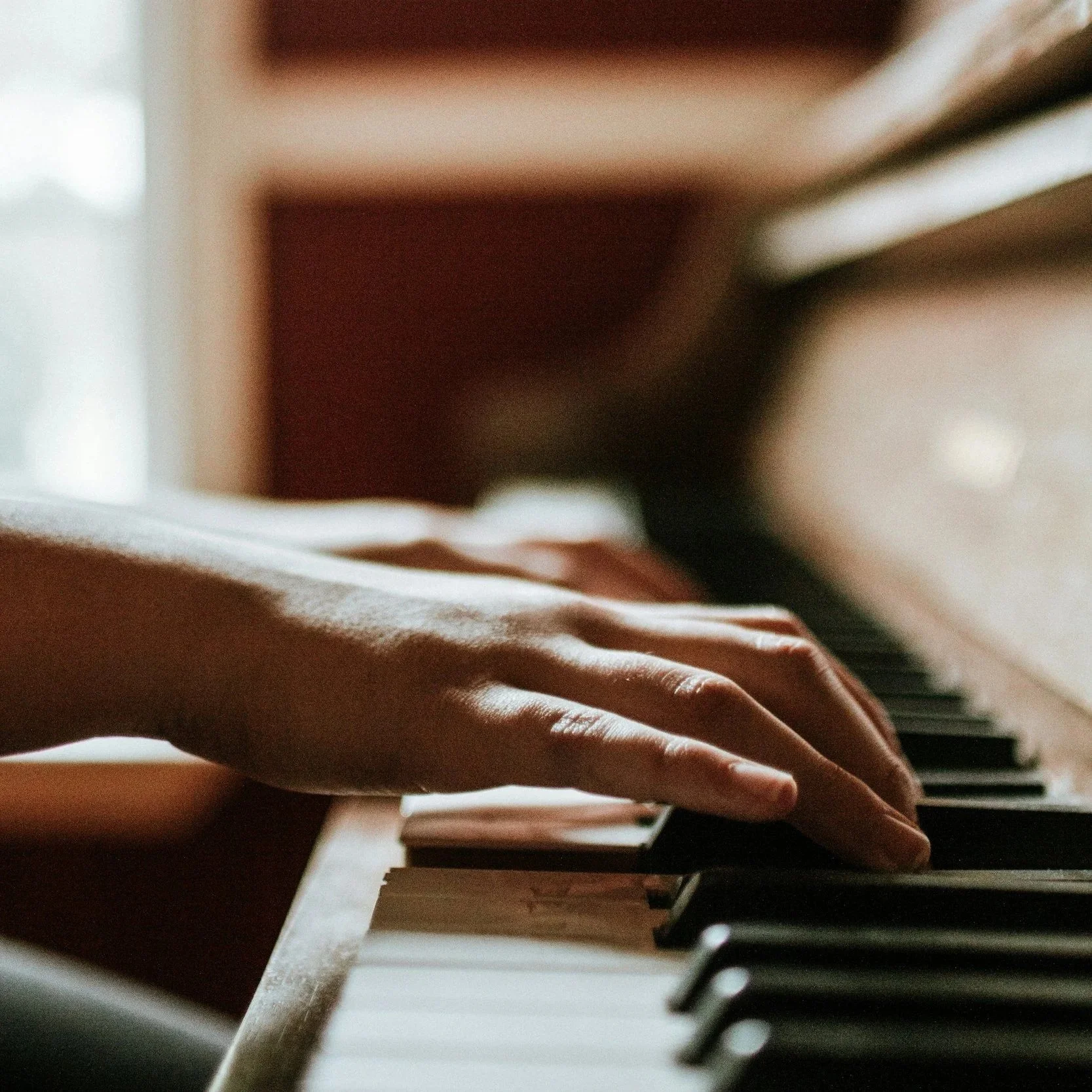 Close-up of a person's hand playing the piano, with focus on their fingers on the black and white keys, in a warmly lit indoor setting.