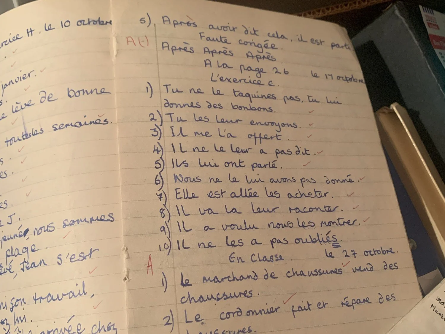 An old French exercise book open at a page of handwritten sentences, marked with red ticks and a red “A”.