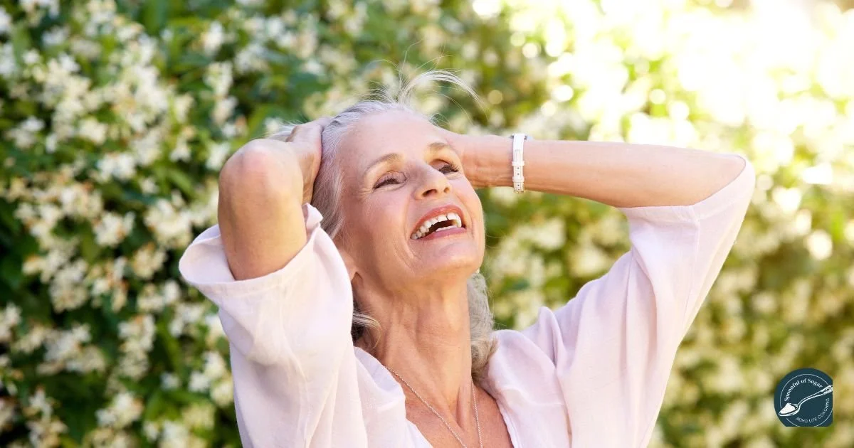 A woman laughing with her hands behind her head in a sunny garden
