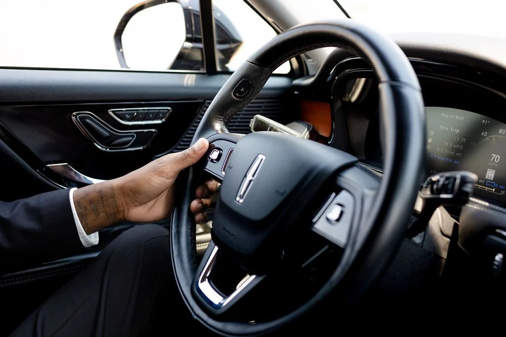Close-up of a person's hand driving a modern car, focusing on the steering wheel and dashboard.