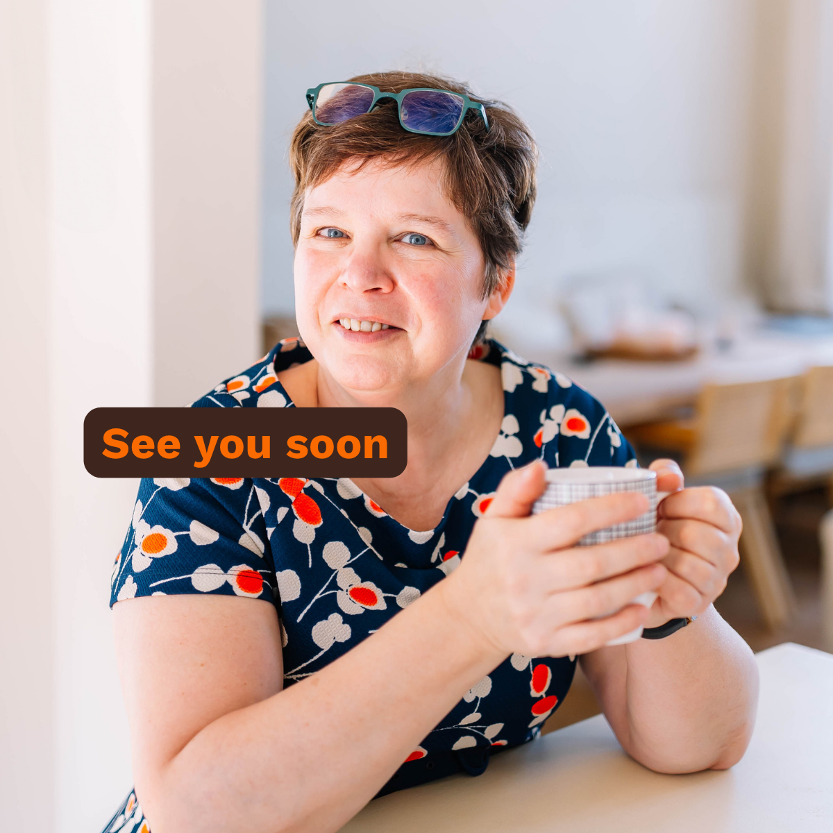 Hilde - oprichtster van 'BRAAZH': Vrouw met kort bruin haar, blauwe ogen, zittend aan tafel met een kopje in haar handen, glimlachend, met een lichte achtergrond. Text overlay: 'See you soon'.