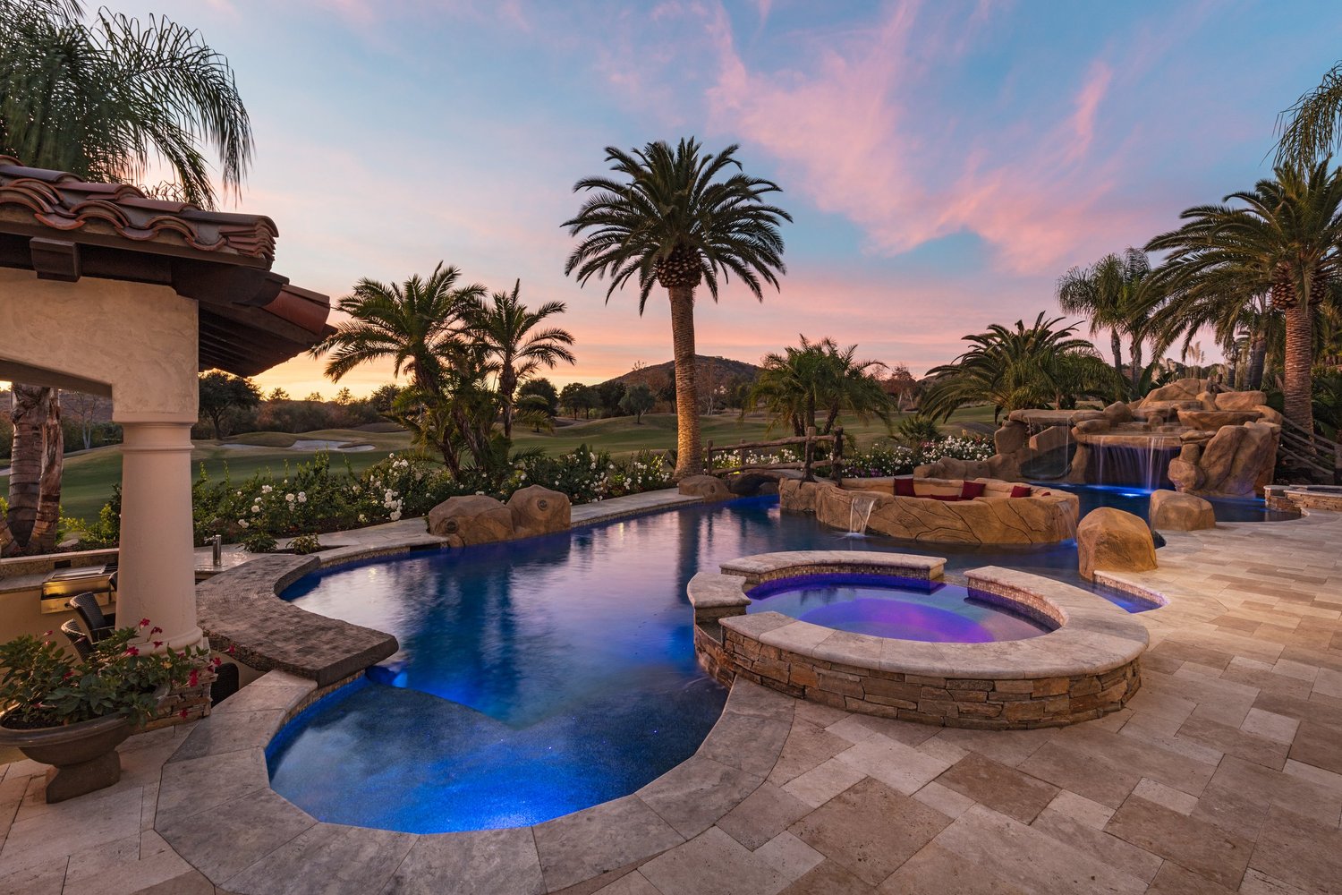 Luxurious backyard with pool, hot tub, palm trees, and sunset view.
