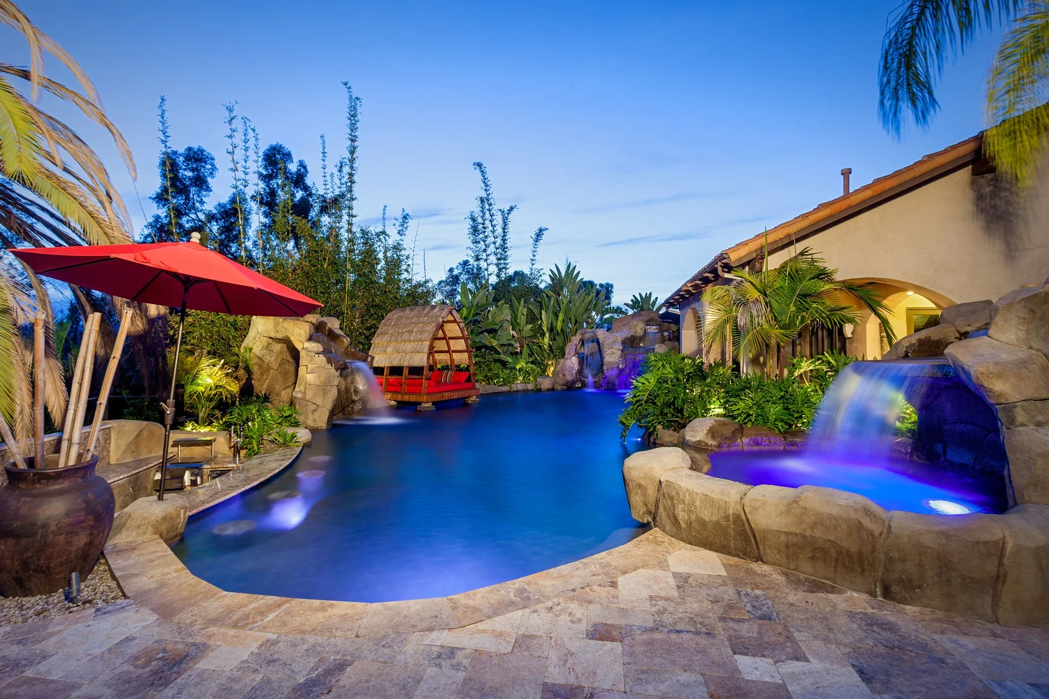 Tropical pool with a thatched pavilion, rock waterfalls and raised spa