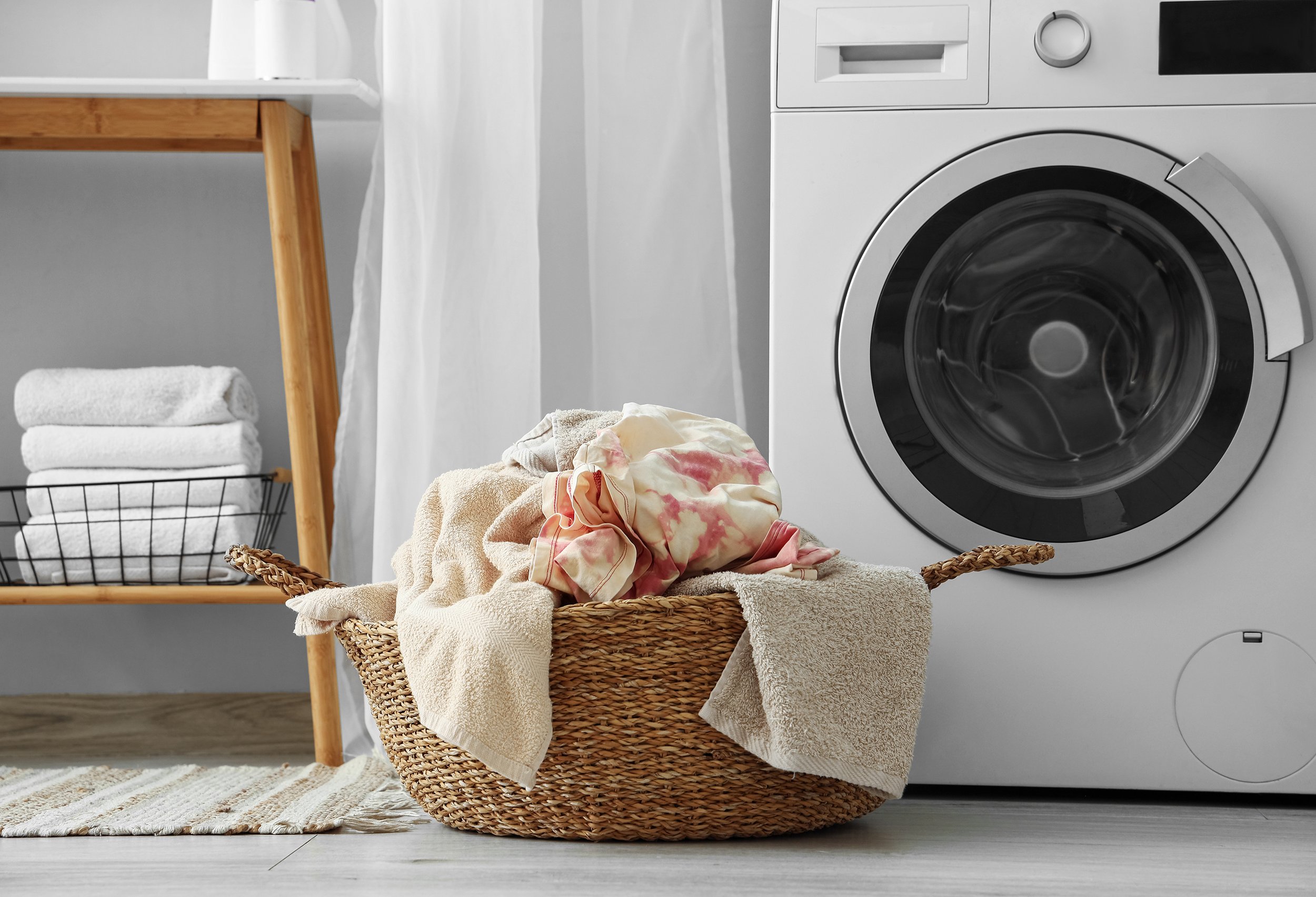 Laundry room with basket of clothes, washing machine, and folded towels on a shelf.