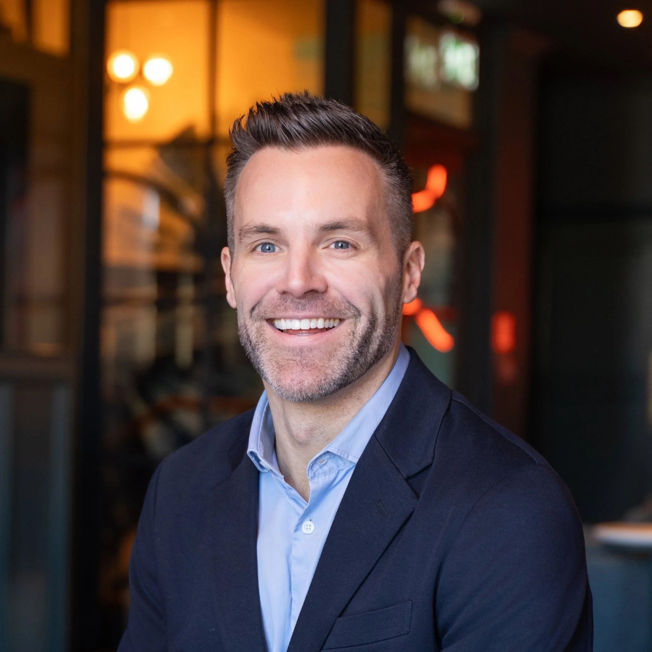 Smiling man in a blazer indoors with warm lighting